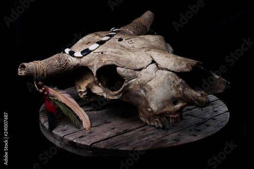 Cow skull decorated with feathers and such, laying on a grey wooden plate, with strong biker / rock n roll / native american vibes.