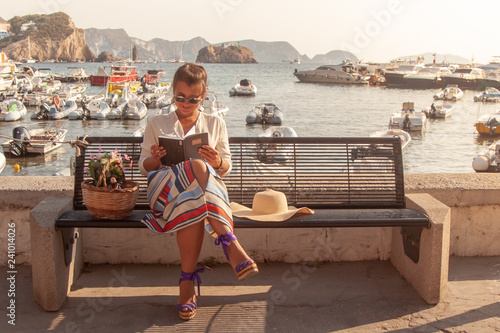 Fotomural Young woman reading book sitting on a bench at the beach