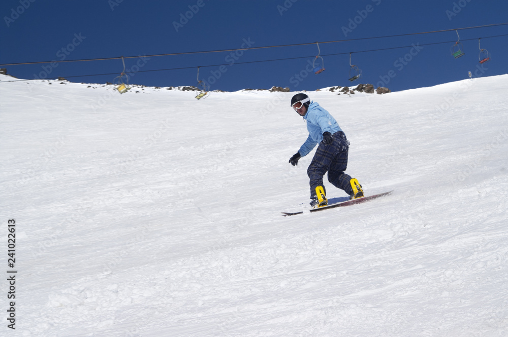 Snowboarder riding on snowy ski slope at high winter mountains in sunny day