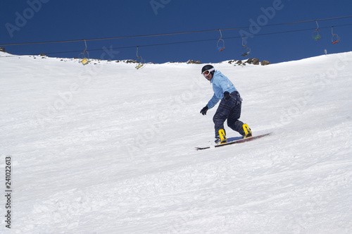 Snowboarder riding on snowy ski slope at high winter mountains in sunny day