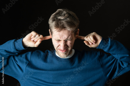 young stressed male protecting his ears from lour irritative noises photo