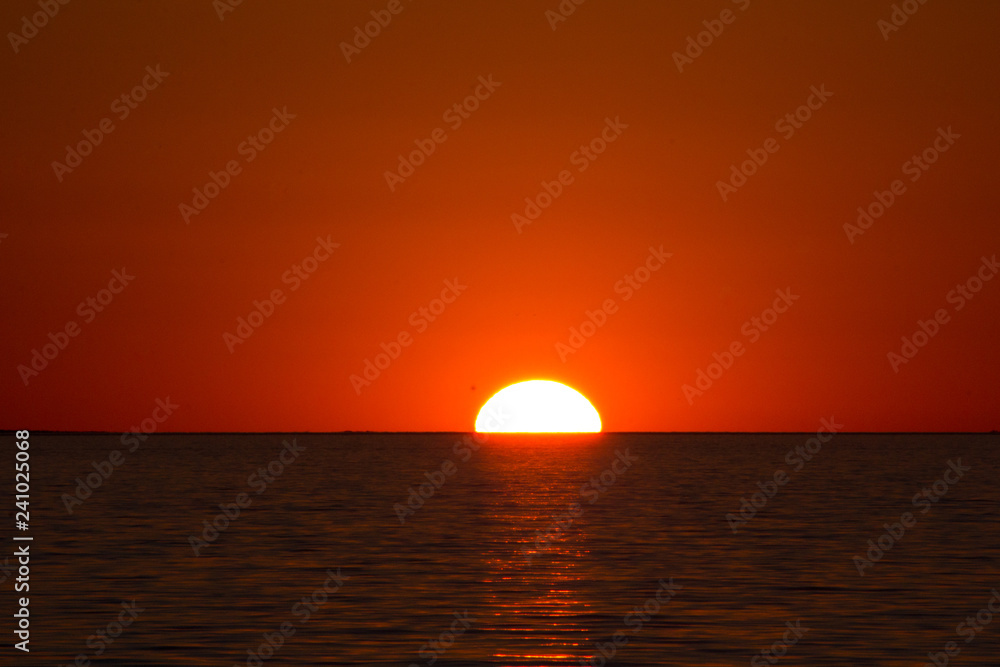 Half red hot African sun setting behind the horizon and a rippled Lake Kariba, Zimbabwe