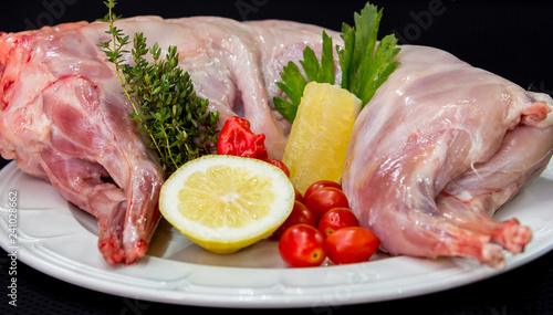 Raw rabbit meat with herbs and spices on a white plate against a black background (ID: 241028662)