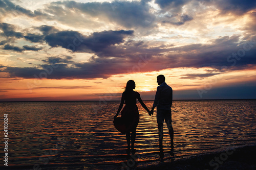Young loving couple holding hands at sunset on the lake