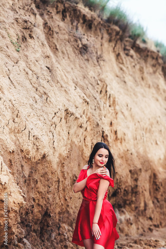 beautiful woman in red dress posing on clay cliff background.