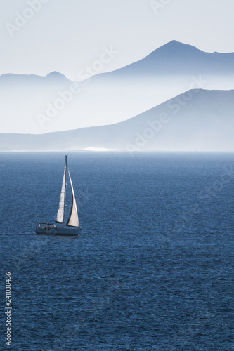 sea with sailboat and mountains of an islan