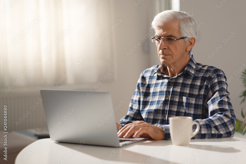 Senior man surfing the internet on laptop in the living room