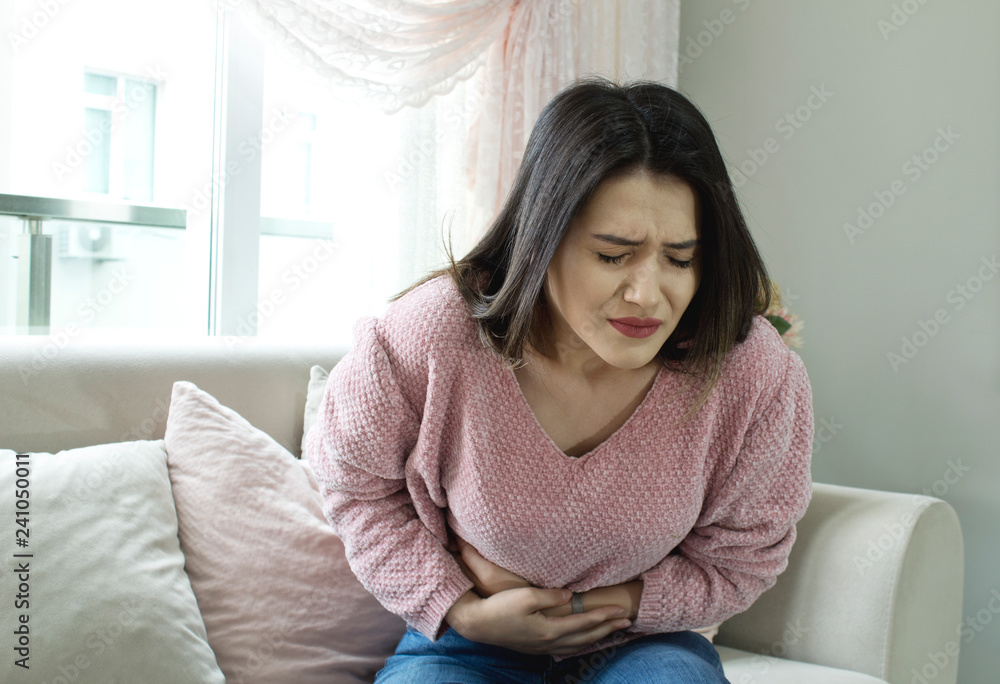 Young woman sitting on the couch suffering from stomach ache at home. Young woman sitting on the couch suffering from stomach ache at home.