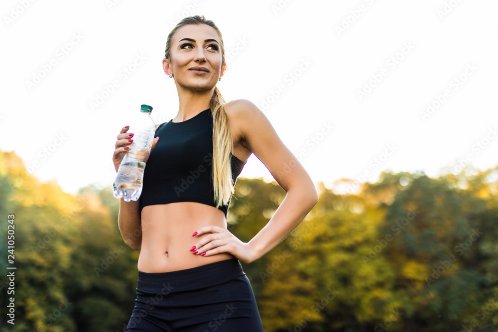 Thirsty woman drinking water to recuperate after jogging in park Thirsty woman drinking water to recuperate after jogging in park