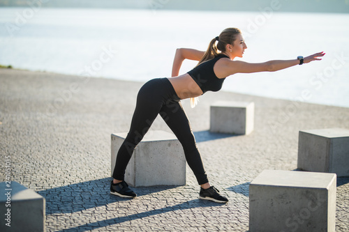 Attractive and strong woman stretching before fitness on the lake in the summer. Sports concept. Healthy lifestyle