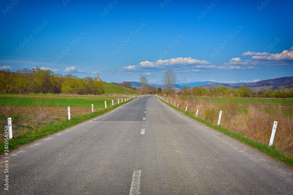 Naklejka premium asphalt road through the green field and clouds on blue sky in summer day