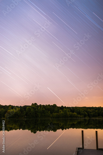 Beautiful nightsky startrails with a view on the dusty milky way overlooking a lake with a dock