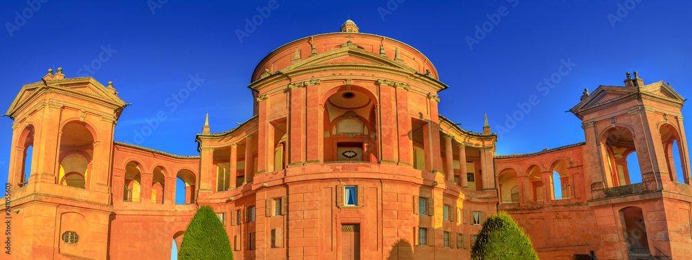 Obraz premium Wide angle panorama San Luca Holy Mary Sanctuary of Bologna at sunset. The Catholic cathedral of San Luca is located on the hills of Bologna city. Sunny with blue sky. Banner cityscape.