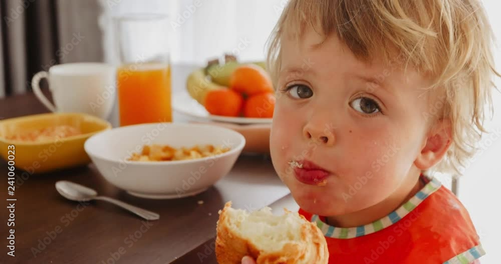 Small child eating croissant at breakfast. Close up of face of toddler little boy eating tasty bun. Head and shoulders portrait. Small child eating croissant at breakfast. Close up of face of toddler little boy eating tasty bun. Head and shoulders portrait.