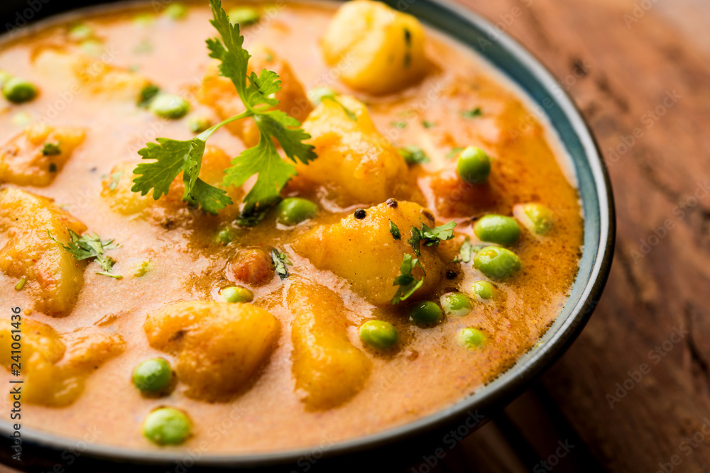 Indian Aloo Mutter curry - Potato and Peas immersed in an Onion Tomato Gravy and garnished with coriander leaves. Served in a Karahi/kadhai or pan or bowl. selective focus Indian Aloo Mutter curry - Potato and Peas immersed in an Onion Tomato Gravy and garnished with coriander leaves. Served in a Karahi/kadhai or pan or bowl. selective focus