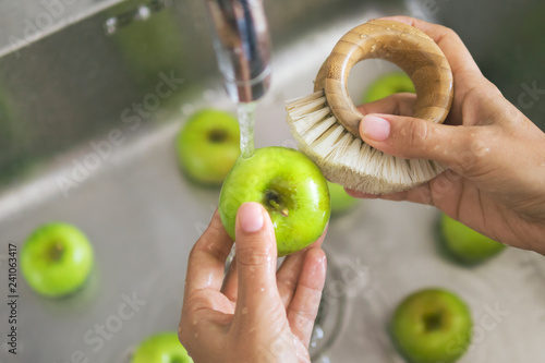 Young Vegan Girl Washing Green Apples with Bamboo Brush. Hand Holding Fresh Fruits Under Running Water in Kitchen Sink. Healthy Lifestyle Hygiene Concept. photo