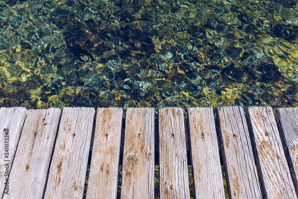 Fototapeta premium Wooden board empty over sea, can be used for display or present a product. Summer season. Empty perspective wooden planks over the reflection of green water, product display template.