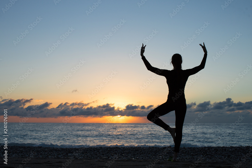 silhouette of woman doing yoga on the beach at sunset