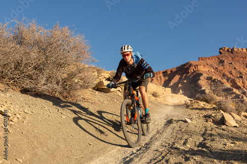 A young man rides a mountain bike down a dirt trail in the desert of Southern Utah on a winter day.