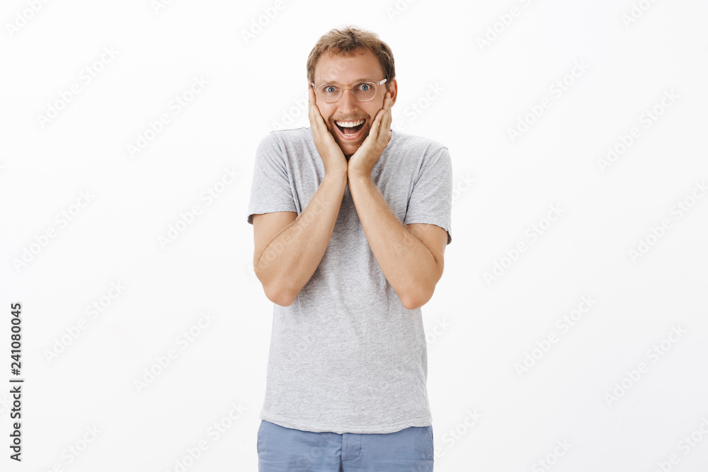 Cannot wait open surprise. Thrilled happy and enthusiastic cute european man with bristle holding palms on jaw and cheeks smiling broadly from excitement hearing excellent news over white wall Cannot wait open surprise. Thrilled happy and enthusiastic cute european man with bristle holding palms on jaw and cheeks smiling broadly from excitement hearing excellent news over white wall