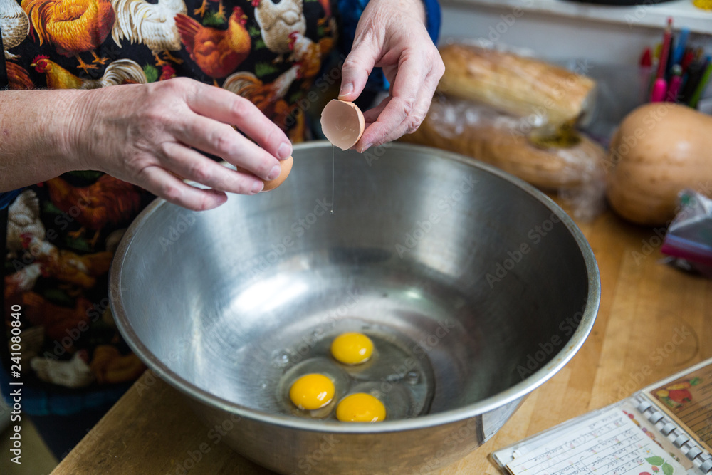 Home baker cracking eggs into a stainless steel mixing bowl for a recipe