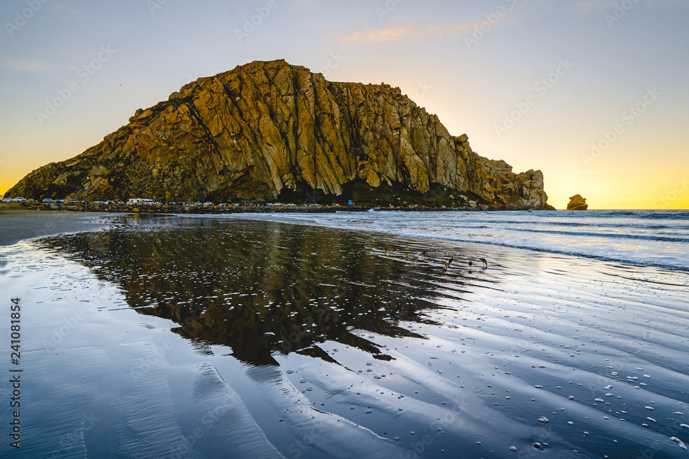 Fototapeta premium Moro Rock in Morro Bay, California, beautiful reflection in the water, blue waves and colorful sky