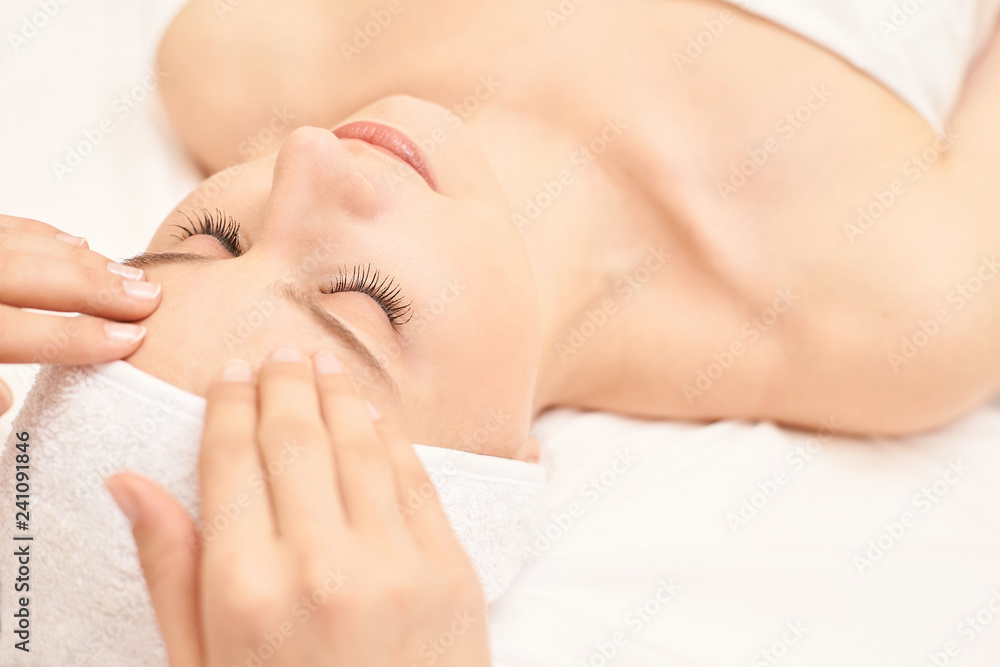 Beauty girl getting face massage at salon. White towel. People hands. Closed eyes