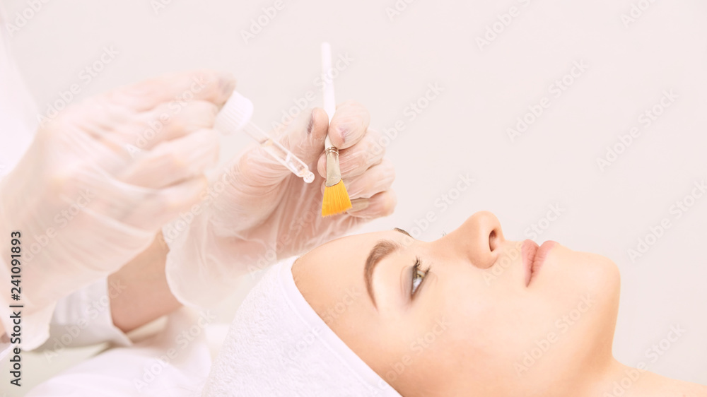 Young woman cleaning face skin in salon. Retinol peel with brush. Acid organic peeling