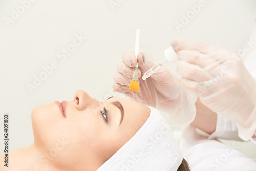 Young woman cleaning face skin in salon. Retinol peel with brush. Acid organic peeling photo