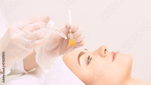 Young woman cleaning face skin in salon. Retinol peel with brush. Acid organic peeling photo