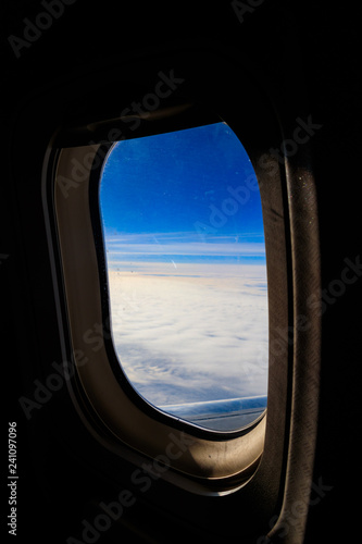 View of blue sky with white clouds through the porthole window flying airplane