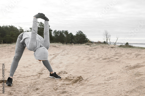 Unrecognizable sportswoman wearing sports clothes standing on sandy beachm keeping feet wide, bending towards, holding hands clasped behind her back. Fitness, leisure, well being and activity photo