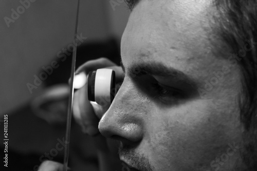 A man looks through a magnifying glass with LED lights on the cutting edge of the knife to check its sharpening.