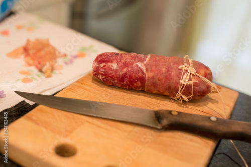 horizontal image with close up detail of a salami on top of a cutting board with a knife near it