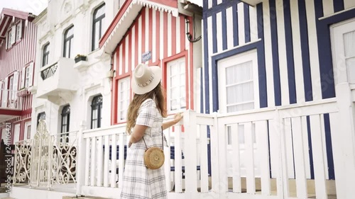 Side view of young female in checkered dress walking along stone road near magnificent colorful houses in Costa Nova, Portugal