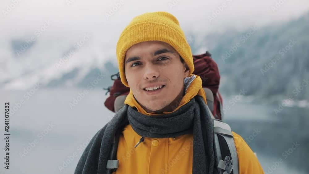 Portrait of a young attractive man in winter clothes. Hiking man wearing yellow winter clothes looks at the camera and smiles. Beautiful mountains and snow-covered lake background Portrait of a young attractive man in winter clothes. Hiking man wearing yellow winter clothes looks at the camera and smiles. Beautiful mountains and snow-covered lake background
