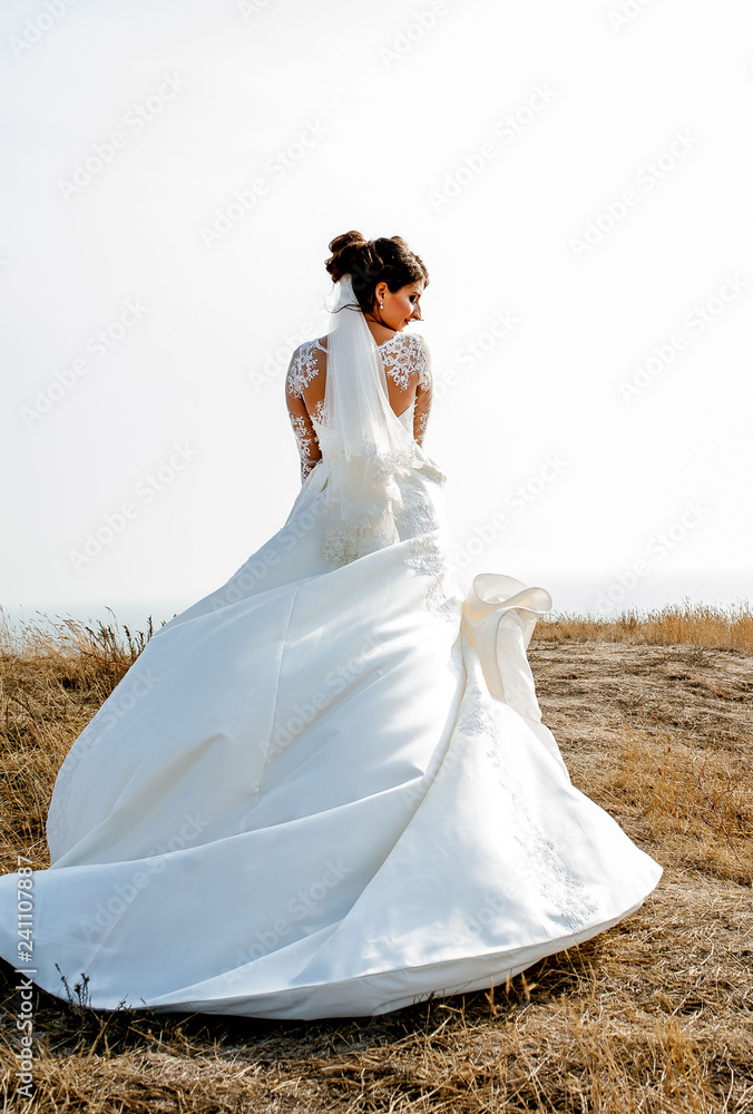 beautiful bride in a wedding dress is standing on the mountainside near the sea and spinning while holding the dress