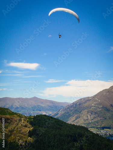 A para glider flying over a big blue lake in the mountains of New Zealand