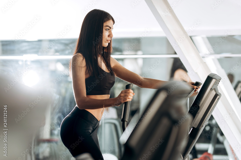 Slim dark-haired girl dressed in black sportswear work out on a treadmill in the gym Slim dark-haired girl dressed in black sportswear work out on a treadmill in the gym
