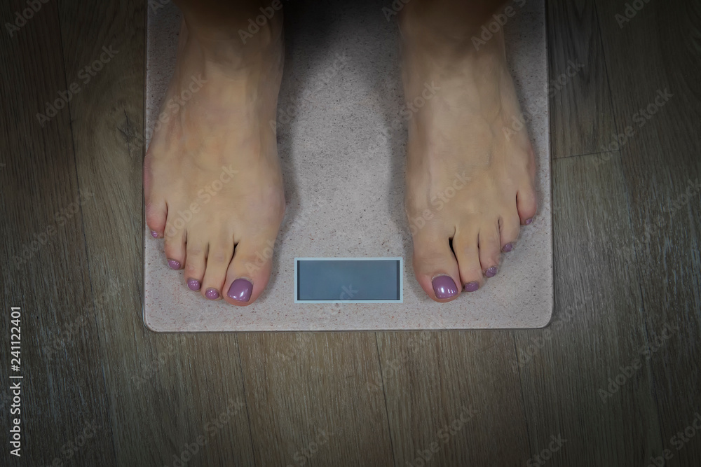 Diet and fitness concept. Close up to female bare feet with pedicure standing on scales with empty display. Woman standing on bathroom scale to check her weight. Weighting. Wellnes and health. - obrazy, fototapety, plakaty 