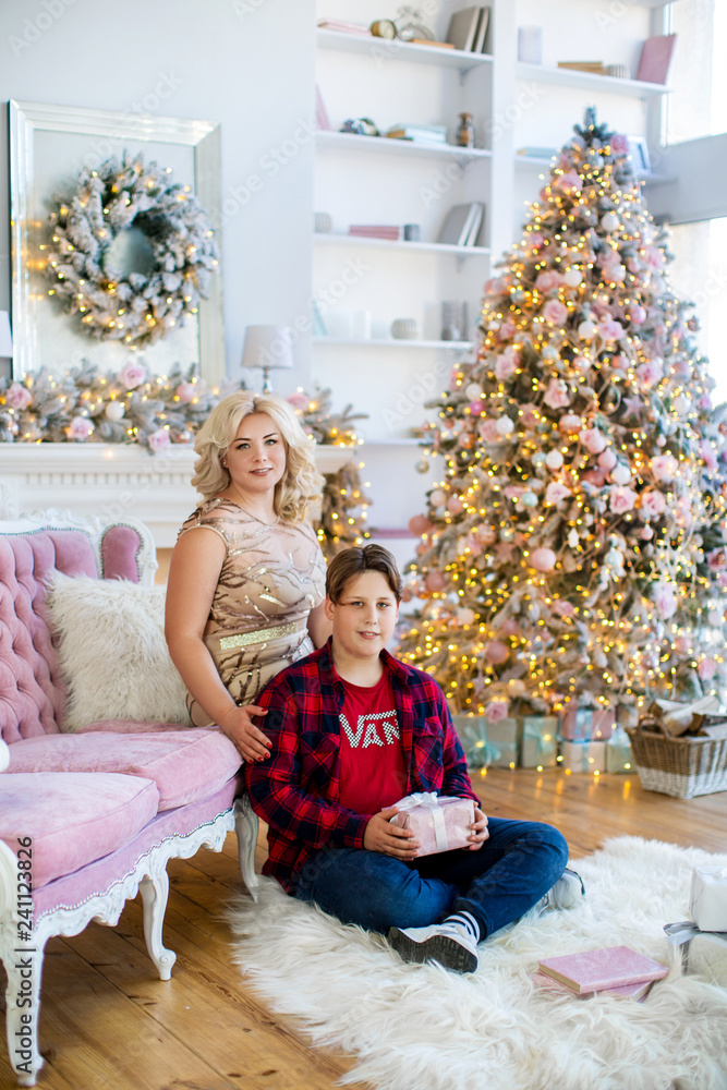 Beautiful mother in luxurious dress and son together in cozy room with Christmas tree and fireplace Beautiful mother in luxurious dress and son together in cozy room with Christmas tree and fireplace