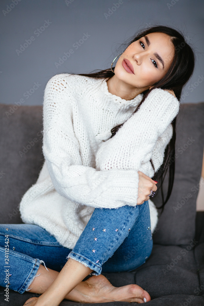 Beautiful girl in a white jacket and jeans is resting on the sofa at home. portrait, scandinavian style