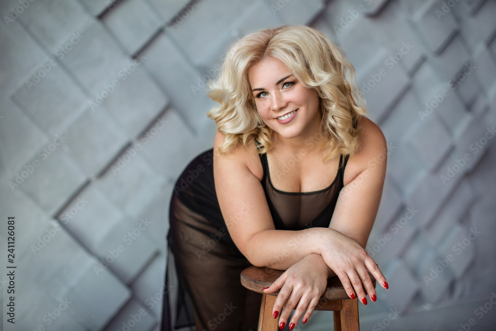 Fototapeta premium Beautiful blonde girl in black dress leaned on chair