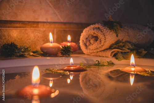 relaxing spa background with candles floating in the bath water, some green petals and a towel near the water surface