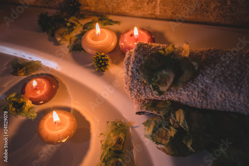 relaxing spa background with candles floating in the bath water, some green petals and a towel near the water surface