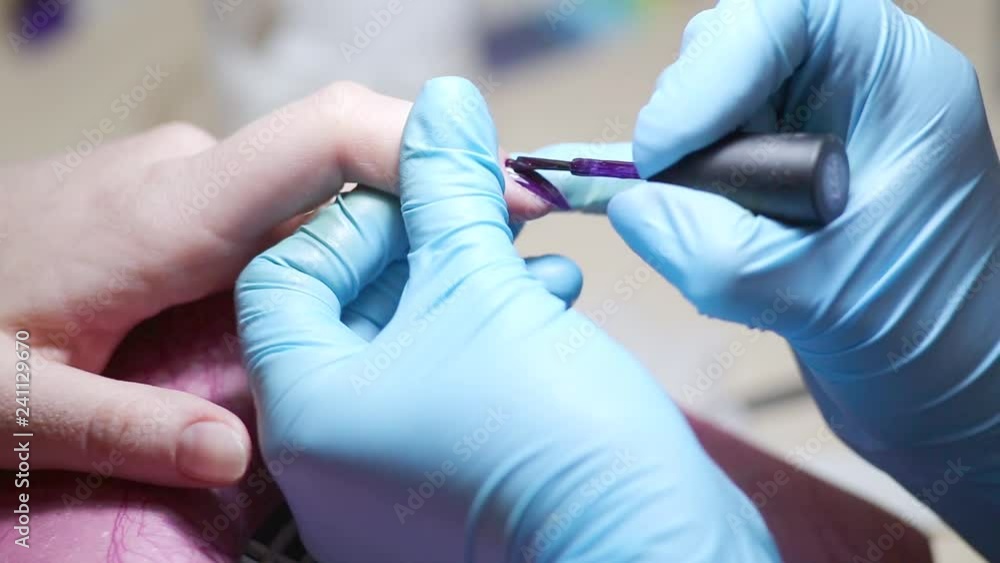 Woman having a manicure of nails in a beauty salon with a close up view of a beautician applying nail polish with an applicator. Master painted nails with varnish. Woman having a manicure of nails in a beauty salon with a close up view of a beautician applying nail polish with an applicator. Master painted nails with varnish.