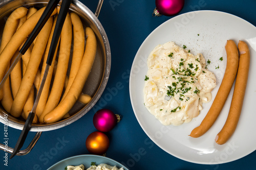 Wiener Würstchen und Kartoffelsalat als typisches Weihnachtsessen zu Heiligabend in Deutschland mit bunten Weihnachtsbaumkugeln und Dekoration