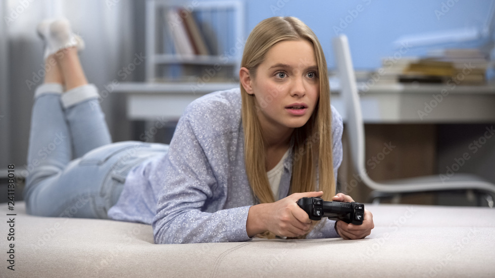Emotional teenage girl playing video game using joystick, youth entertainment