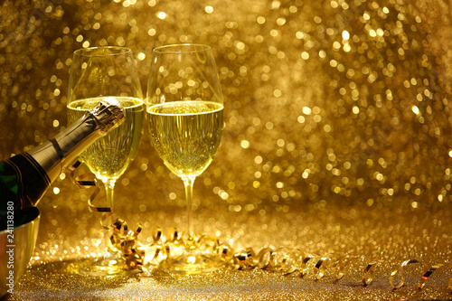 Kieliszki i butelka z szampanem na złotym, błyszczącym tle.