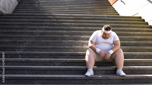 Obraz na płótnie Upset man sitting alone on stairs, fighting with overweight and food addiction